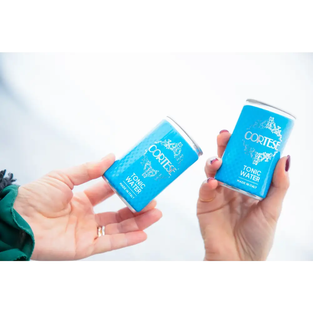 Mano femminile con due lattine di Cortese Tonic Water – tonica artigianale italiana ideale per gin tonic e aperitivi