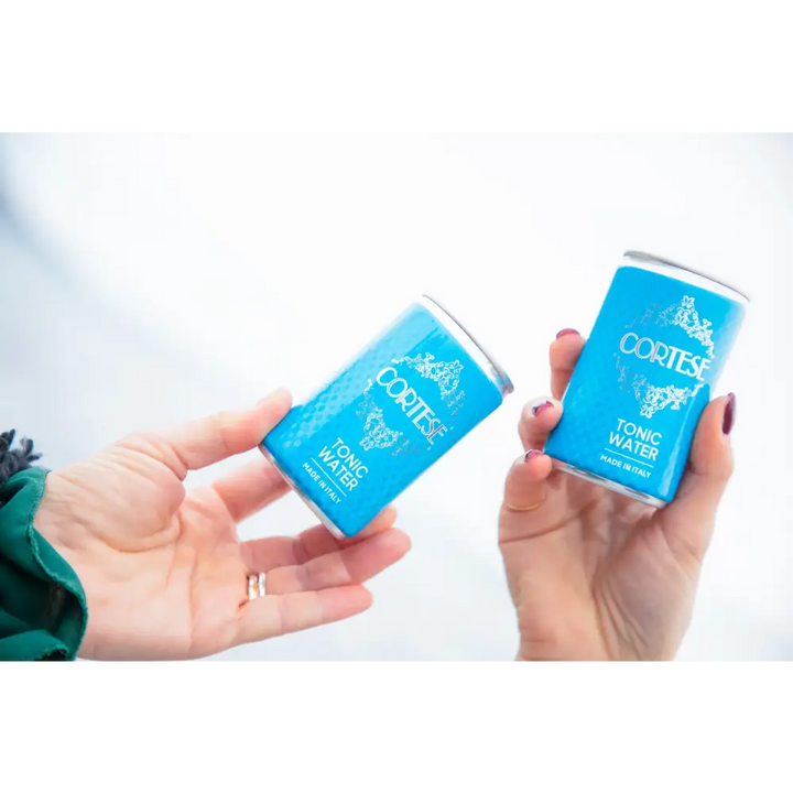 Mano femminile con due lattine di Cortese Tonic Water – tonica artigianale italiana ideale per gin tonic e aperitivi