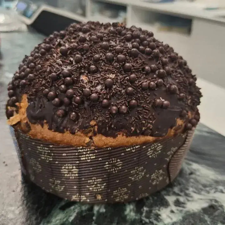 Panettone artigianale al cioccolato ricoperto di scaglie e perle di cioccolato fondente, fotografato in pasticceria